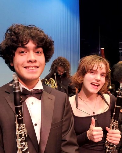 Two AYO woodwind players in concert attire give a thumbs up backstage